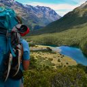 Rear View Of Young Man With Backpack Standing On Mountain Against Sky